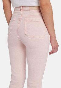 Jean taille haute rose clair avec un design ajusté, comprenant deux poches arrière et des détails de couture subtils. Texture en denim lisse.