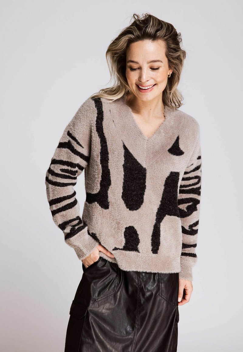 Beige sweater with black abstract animal print, V-neck, long sleeves. Soft texture and relaxed fit, paired with a black leather skirt.