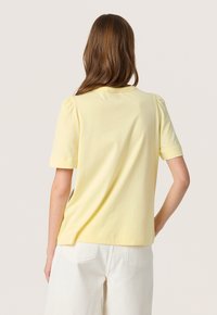 Tricou din bumbac galben pal, cu mâneci scurte și decolteu rotund. Ușor strâns la cusăturile umerilor, textură moale și tăietură lejeră.
