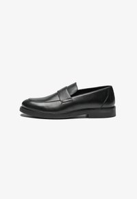 Schwarze Lederloafer mit flacher Sohle, ausgestattet mit einem gesteppten Design und einem Band über dem Vorderfuß für zusätzliche Details. Glatte Textur über die gesamte Fläche.