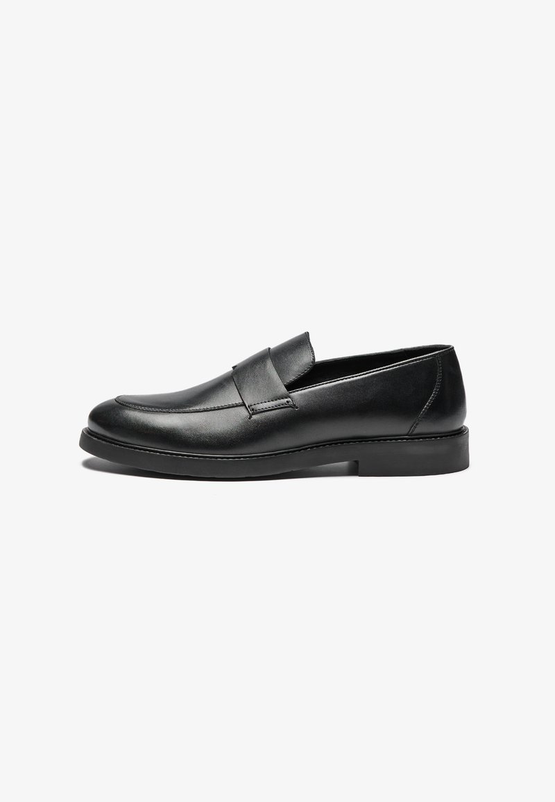 Schwarze Lederloafer mit flacher Sohle, ausgestattet mit einem gesteppten Design und einem Band über dem Vorderfuß für zusätzliche Details. Glatte Textur über die gesamte Fläche.