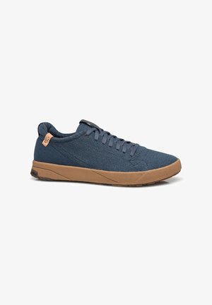 Zapatillas de tela azul texturizada con una suela de goma marrón, que cuentan con cordones y un pequeño detalle de logo en el talón.
