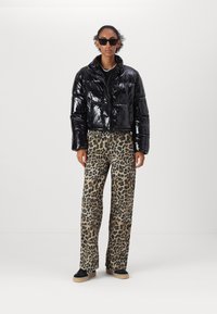 Černá lesklá zkrácená puffer bunda přes černý top, doplněná kalhotami s leopardím potiskem a černými platformovými teniskami.