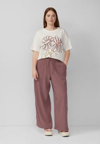 Marseillan fit, crèmekleurig graphic t-shirt met bloemmotief in kastanjebruin. Gecombineerd met losse, gemêleerde, roestkleurige broeken en platform sandalen.