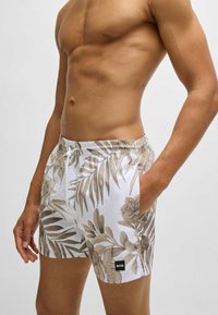 Weiße Badehose mit einem hellbraunen Palmblattmuster, elastischem Bund, Seitentaschen und einem Logo-Tag an der unteren Seite.