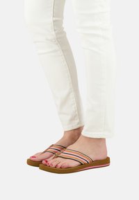 Strappy flip-flops with a brown rubber sole and colorful horizontal stripes on the strap. Paired with white fitted jeans.