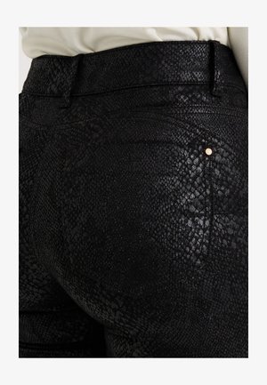 Pantalones negros con textura y patrón de piel de reptil. Cuentan con una cintura ajustada y un pequeño detalle dorado cerca del bolsillo trasero. Material suave y brillante.