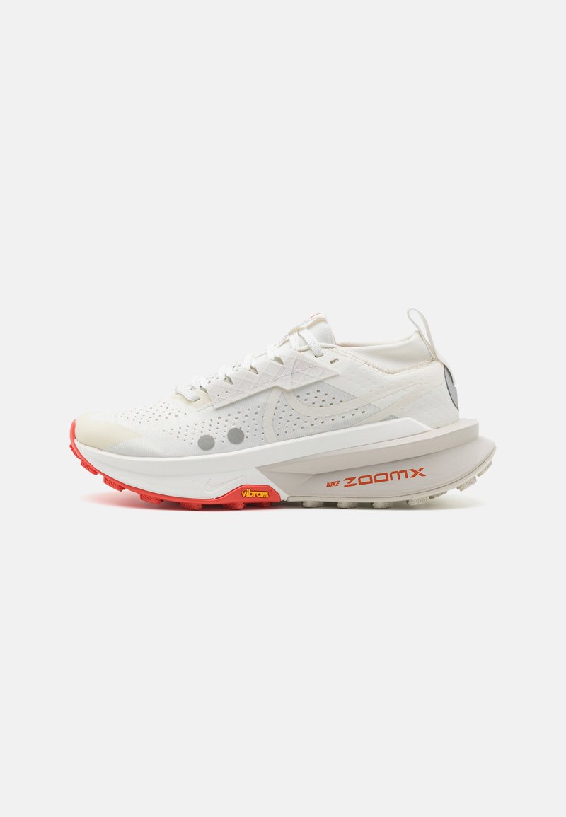 Chaussure de sport blanche avec une tige en maille respirante, semelle extérieure rouge, marque Nike ZoomX bien en vue et accents réfléchissants. Présente des détails perforés.