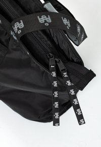 Czarna torba materiałowa z dwoma suwakami i czarnymi paskami, ozdobiona białym powtarzającym się abstrakcyjnym wzorem logo.