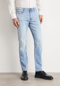 Světle modré džíny z denimu s úzkým střihem, vybledlou texturou, designem s pěti kapsami a kontrastním prošíváním. Doplněné černými šněrovacími botami.