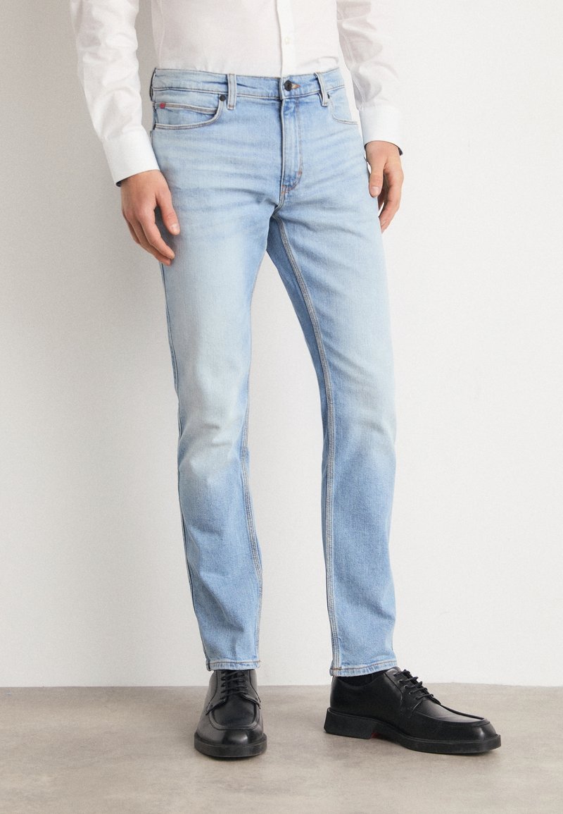 Světle modré džíny z denimu s úzkým střihem, vybledlou texturou, designem s pěti kapsami a kontrastním prošíváním. Doplněné černými šněrovacími botami.