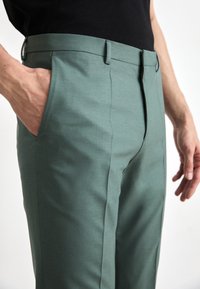 Groene op maat gemaakte broek van soepel materiaal, met zijzakken, een vlakke voorkant en een slank model met een subtiele glans.