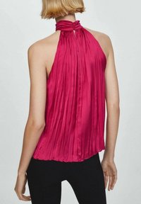 Top halter plissettato in magenta vivace. Presenta un colletto arricciato, un tessuto fluido e una vestibilità ampia. Indossato con pantaloni neri, che mettono in evidenza dettagli strutturati.