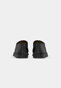 Une paire de chaussures de ville en cuir noir montrées de l'arrière sur un fond blanc uni.