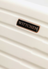 Wittchen brand logo plaque on a cream-colored hard shell suitcase with horizontal ridges.