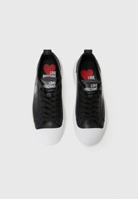 Zwarte leren sneakers met witte rubberen zolen. Heeft zwarte veters en branding op de tong. Interieur heeft een rood-wit "LOVE MOSCHINO" print.