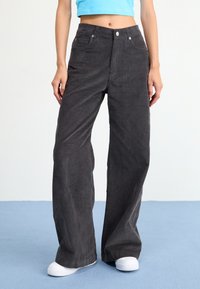 Wide-leg, dark gray corduroy pants with front pockets and a button closure. Worn with a cropped blue top and white sneakers.