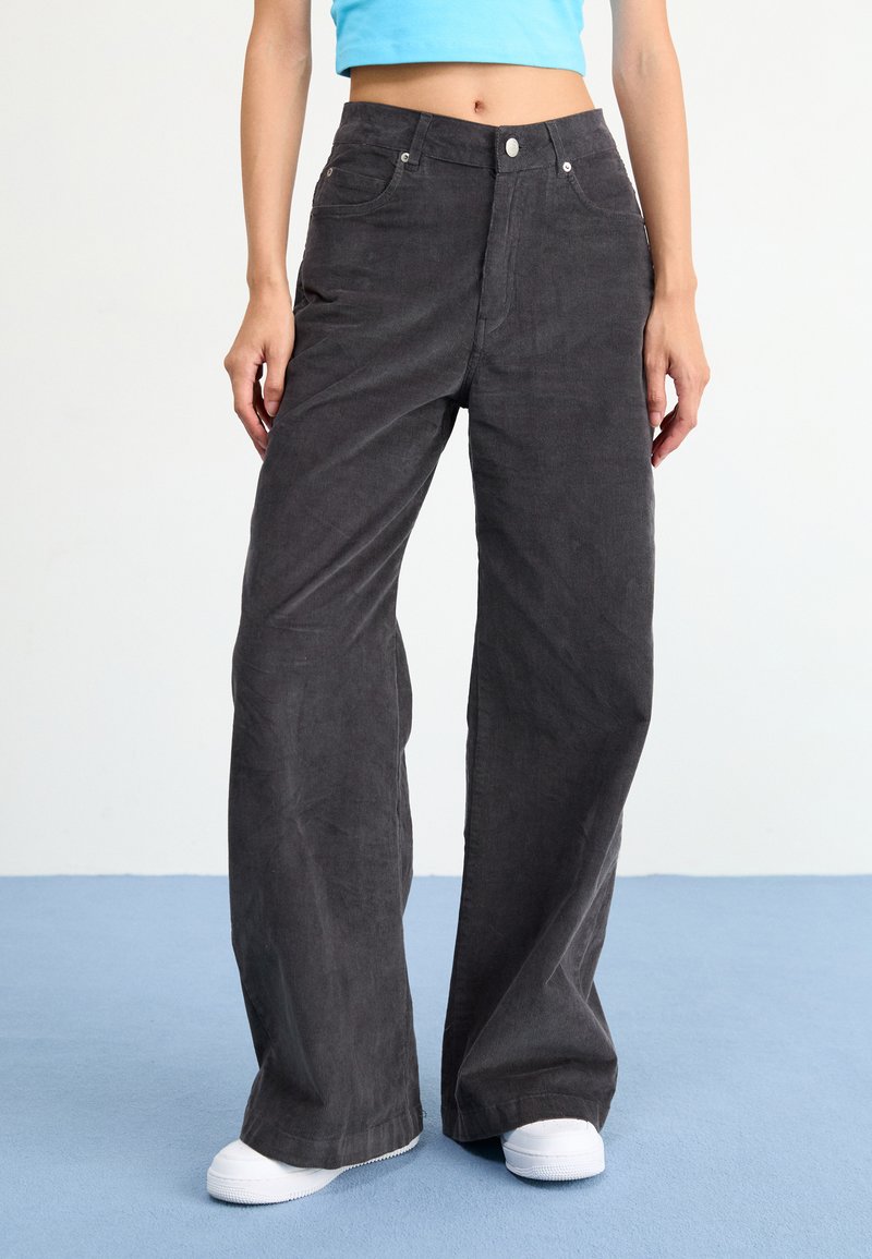 Wide-leg, dark gray corduroy pants with front pockets and a button closure. Worn with a cropped blue top and white sneakers.