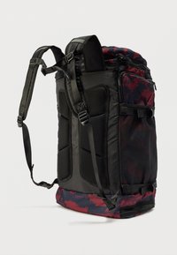 Μαύρο και μαρόν σακίδιο με επένδυση από πλέγμα στα λουριά, πολλές θήκες με φερμουάρ και υφή στον πάτο. Διαθέτει ένα έντονο, αφηρημένο σχέδιο.