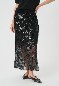 Jupe midi noire avec des embellissements en sequins floraux et un superposition transparente. Fini avec une coupe droite et un ourlet juste sous le genou.