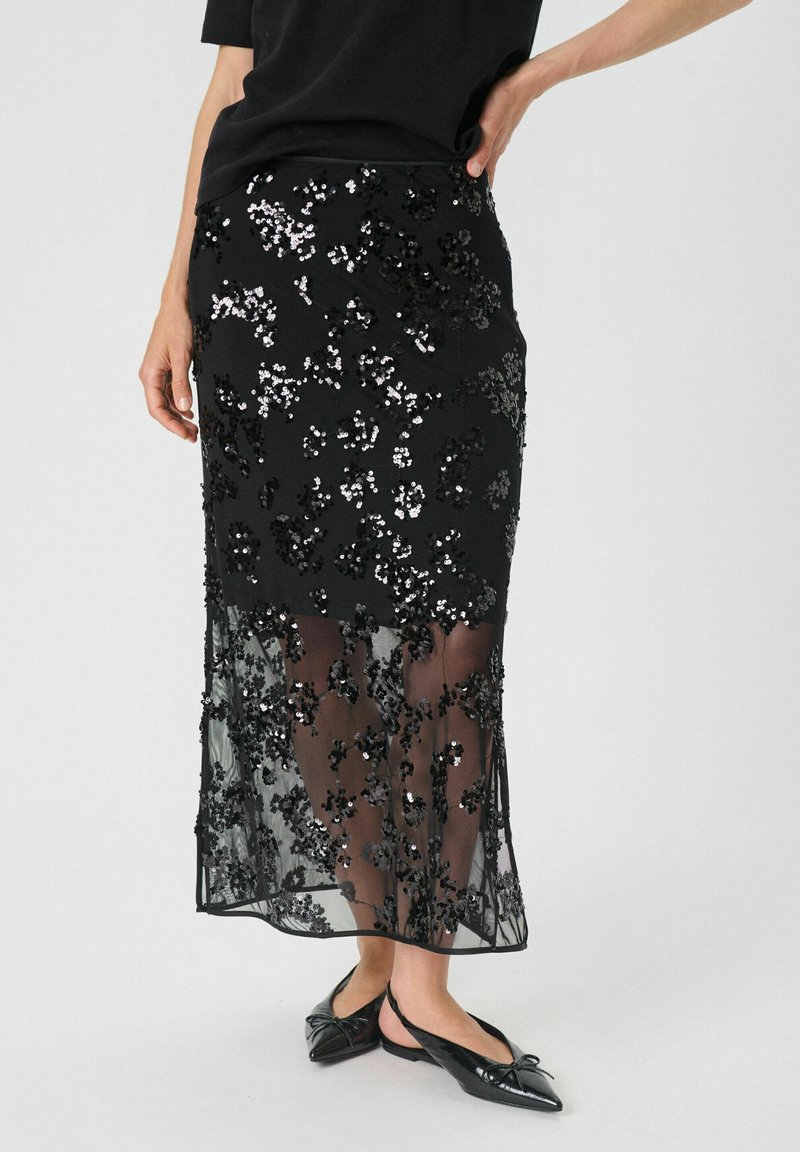 Jupe midi noire avec des embellissements en sequins floraux et un superposition transparente. Fini avec une coupe droite et un ourlet juste sous le genou.