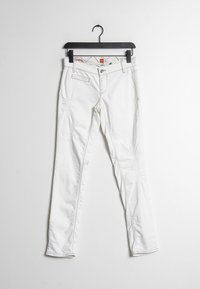 Pantalones de mezclilla blancos con corte slim, con un ligero desgaste, cinco bolsillos y costuras en contraste. Colgados de una percha negra.