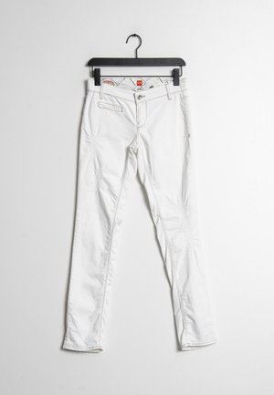 Weiße Denim-Hose mit slim fit, dezenter Gebrauchsspuren, fünf Taschen und kontrastierenden Nähten. Hängt an einem schwarzen Kleiderbügel.