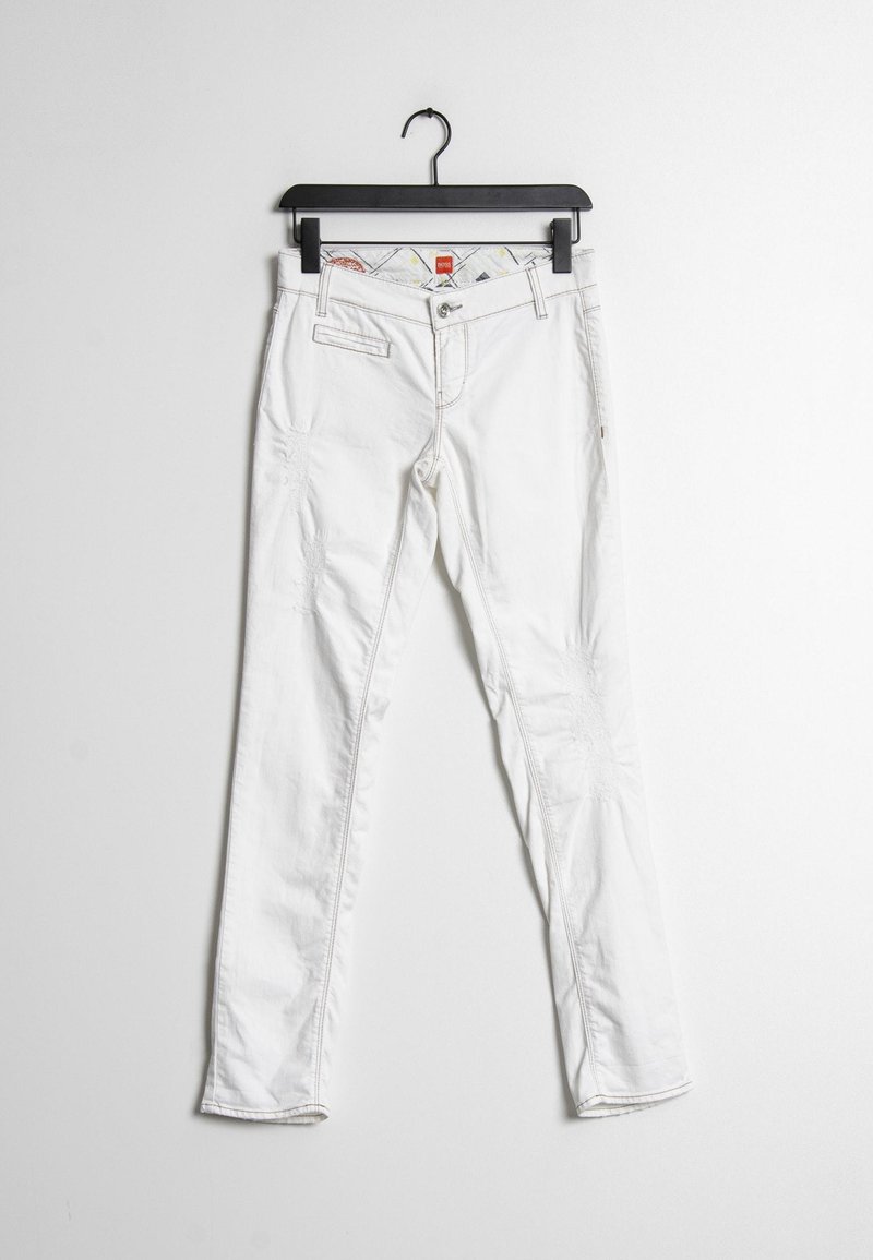 Pantalones de mezclilla blancos con corte slim, con un ligero desgaste, cinco bolsillos y costuras en contraste. Colgados de una percha negra.