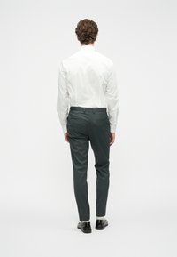 Λευκό πουκάμισο μακρυμάνικο με απαλό υλικό, σε συνδυασμό με σκούρες γκρι παντελόνες κουμπωτές. Το σύνολο έχει slim fit και ελάχιστες λεπτομέρειες.