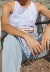 Lila ja valge sidrunitrükkiga crop top, millel on kuldnokk ja logo, koos helesiniste kõrge vöökohaga teksadega. Sile kangas.