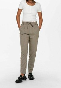 Rutiga, beige och bruna byxor med dragsko i midjan, fickor, tapered passform och en mjuk textur, tillsammans med svarta skor.