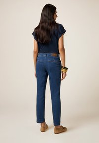 Donkerblauwe jeans met een rechte snit, standaard achterzakken en een leren label op de tailleband. Draagt met een marineblauw top en bruine schoenen.