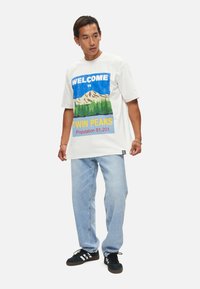 Witte katoenen t-shirt met een kleurrijke grafische print van bergen en bomen, met de tekst "Welkom in Twin Peaks" en "Bevolking 51.201."