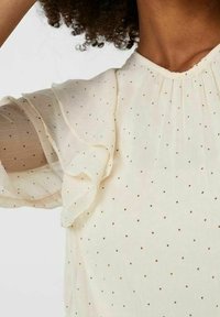 Gennemsigtig cremefarvet bluse med korte, flæseærmer og små, metalliske polka dots. Blød tekstur med en delikat detalje ved halsudskæringen.