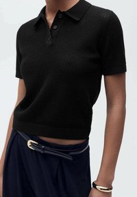 Polo noir à manches courtes en maille texturée avec un col à revers et une patte de boutonnage à trois boutons, associé à un pantalon bleu marine taille haute et une ceinture.