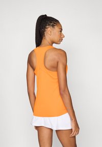 Camiseta deportiva sin mangas naranja con diseño de espalda de nadador, textura suave y silueta ajustada, combinada con una falda blanca de varias capas.