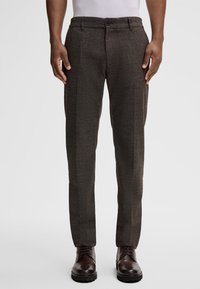Bruine textuurbroek met een slim fit, voorzien van een knoopsluiting en zijzakken. In combinatie met donkere geklede schoenen.