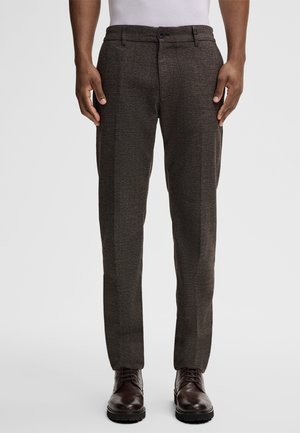 Brown textured trousers with a slim fit, featuring a button closure and side pockets. Paired with dark dress shoes.