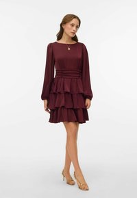 Obleka bordo barve z več plastmi, dolgimi rokavi, nabranim pasom in naborki ob robu. Gladek tekstura z zadržanim ladijskim izrezom.