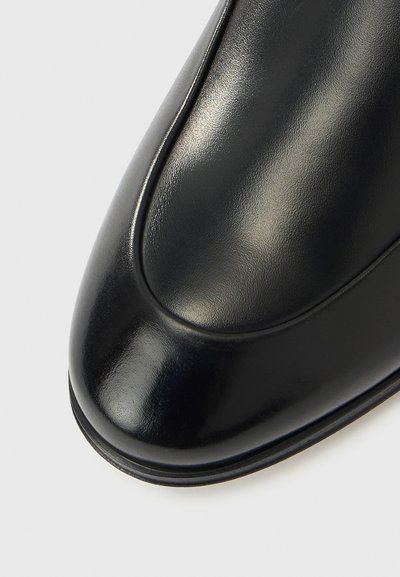 Μαύρο δερμάτινο παπούτσι με λεία, γυαλιστερή επιφάνεια, στρο γγυλεμένη μύτη και διακριτική ραφή κατά μήκος των άκρων.