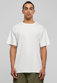 Tricou alb din bumbac cu guler rotund, mâneci scurte și croi lejer. Textură netedă, cu cusături minime și fără modele vizibile.