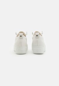 Weiße Leder-Sneaker mit strukturiertem Obermaterial, glatter weißer Sohle, geprägtem Logo an der Ferse und dünnen Ziehlaschen auf der Rückseite.