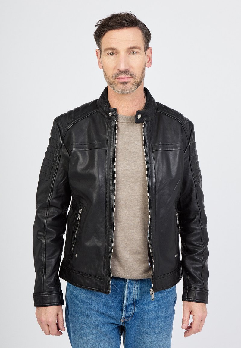 Sort lædermotorcykeljakke med quiltede skulderdetaljer, lynlåslukning foran og to sidelommer, båret over en lys grå skjorte.