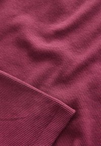 Tissu bordeaux côtelé avec une texture lisse, doté d'un ourlet présentant un motif côtelé uniforme et une légère variation de teinte.