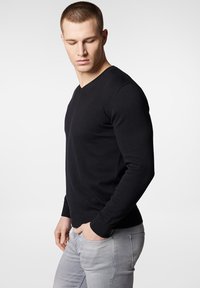 Czarny sweter z dekoltem w serek o żebrowej fakturze, dopasowany krój z długimi rękawami, w połączeniu z jasnoszarymi dżinsami. Czysty, minimalistyczny design.