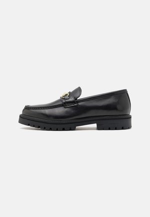 Black leather loafers with a smooth finish, round toe, a decorative strap with gold hardware, and a rugged black sole.