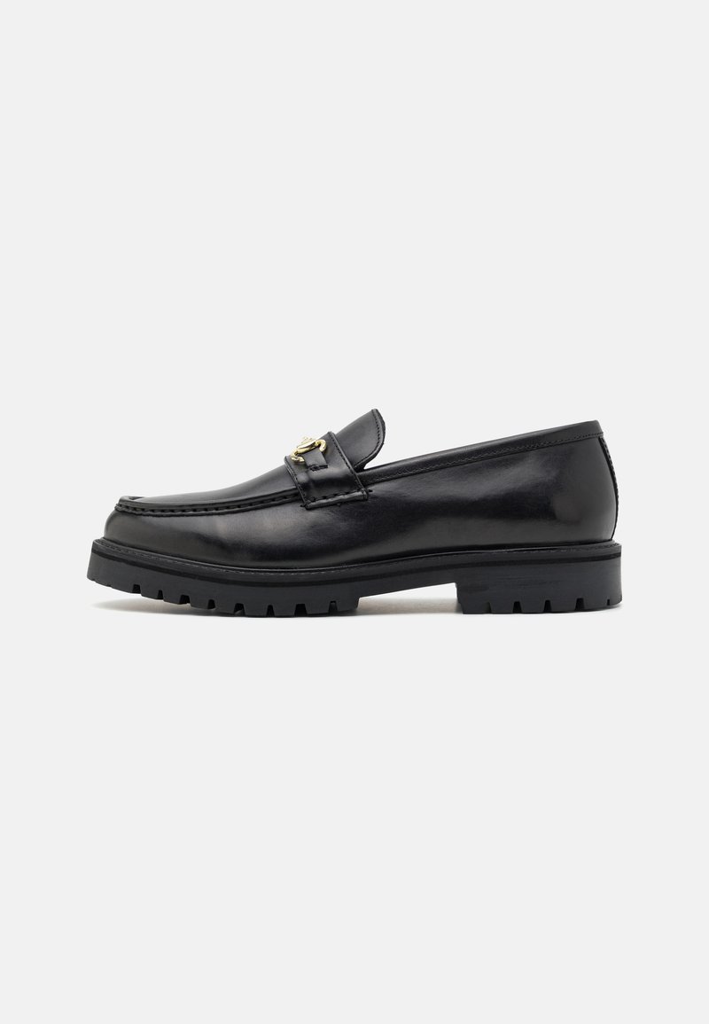 Mocasines de cuero negro con un acabado suave, punta redonda, una tira decorativa con herraje dorado y una suela negra robusta.