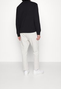 Sudadera negra de mangas largas con dobladillo acanalado, combinada con pantalones beige claros. El calzado son zapatillas blancas. Diseño simple y moderno.