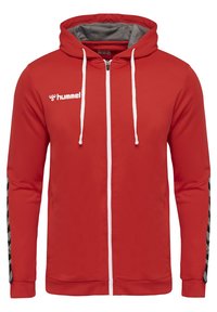 Haut à zip rouge en tissu texturé. Équipé d'une capuche doublée en gris, de cordons blancs et d'accents noir et blanc sur les manches.