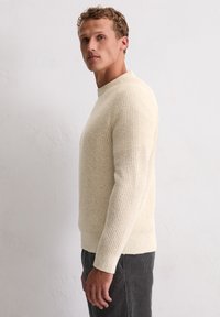 Hellbeige, gestreifter Pullover mit Rundhalsausschnitt, strukturierter Strickmuster und figurschmeichelnder Silhouette. Angenehme Passform, kombiniert mit dunkelgrauen Cordhosen.